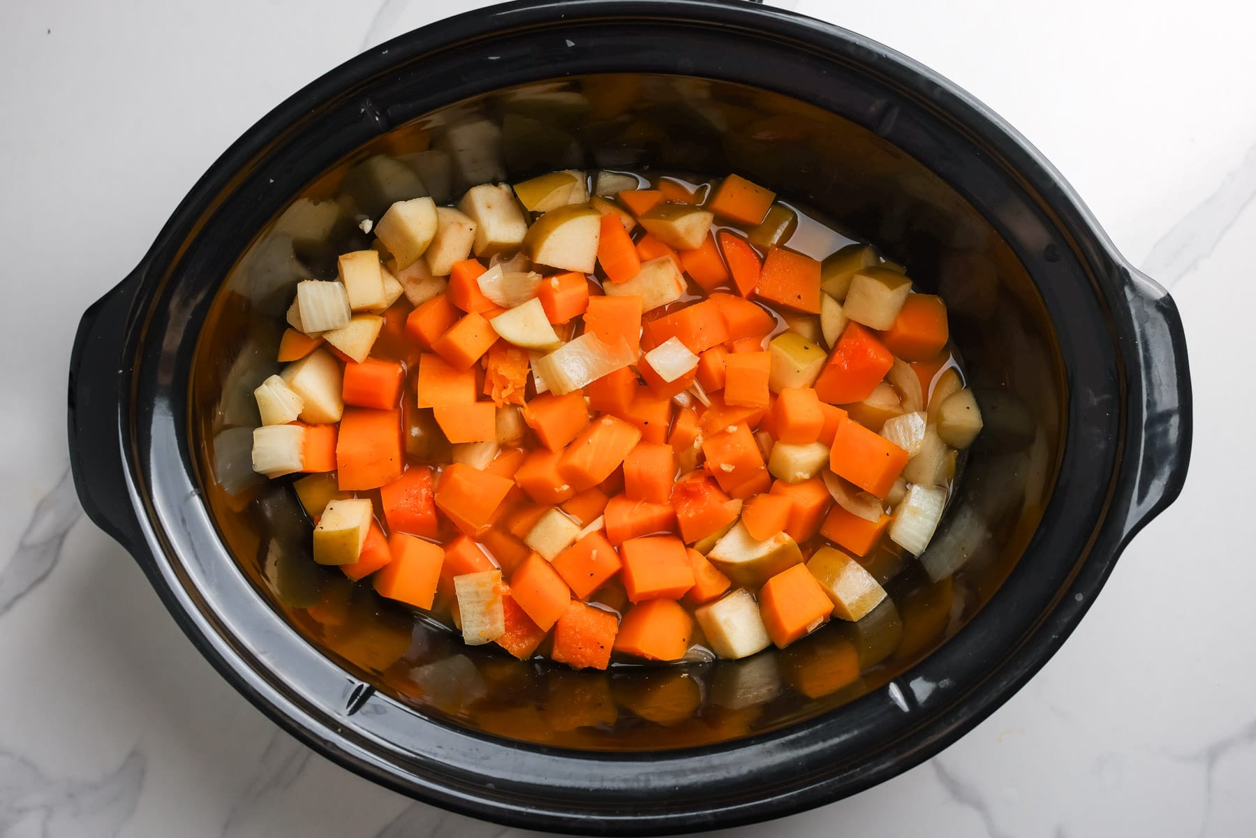 Cooked butternut squash, apples, carrot, and onion in stock in the slow cooker.
