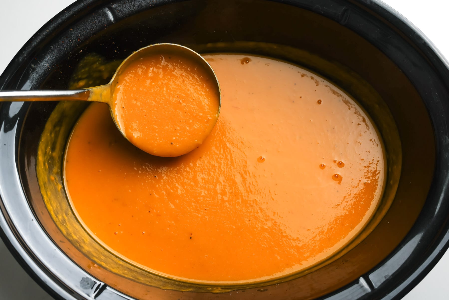 A ladle of smooth blended butternut squash apple soup in the slow cooker after stirring in the coconut milk.