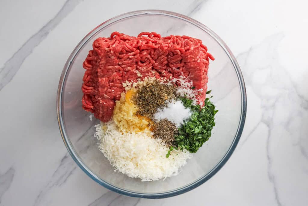 Ground beef, breadcrumbs, and seasonings in a glass mixing bowl.