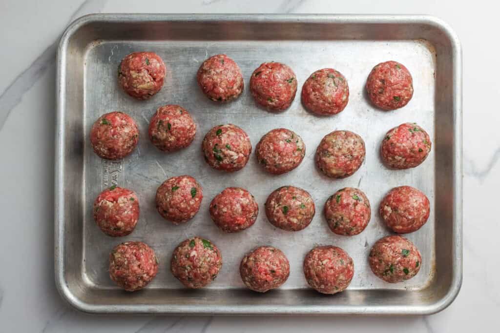 Raw meatballs arranged on a metal baking sheet.