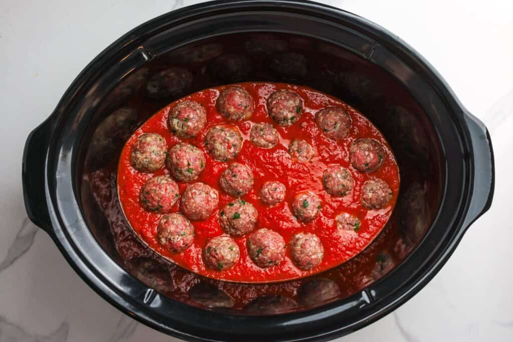 Raw meatballs arranged in a single layer over marinara sauce in a slow cooker