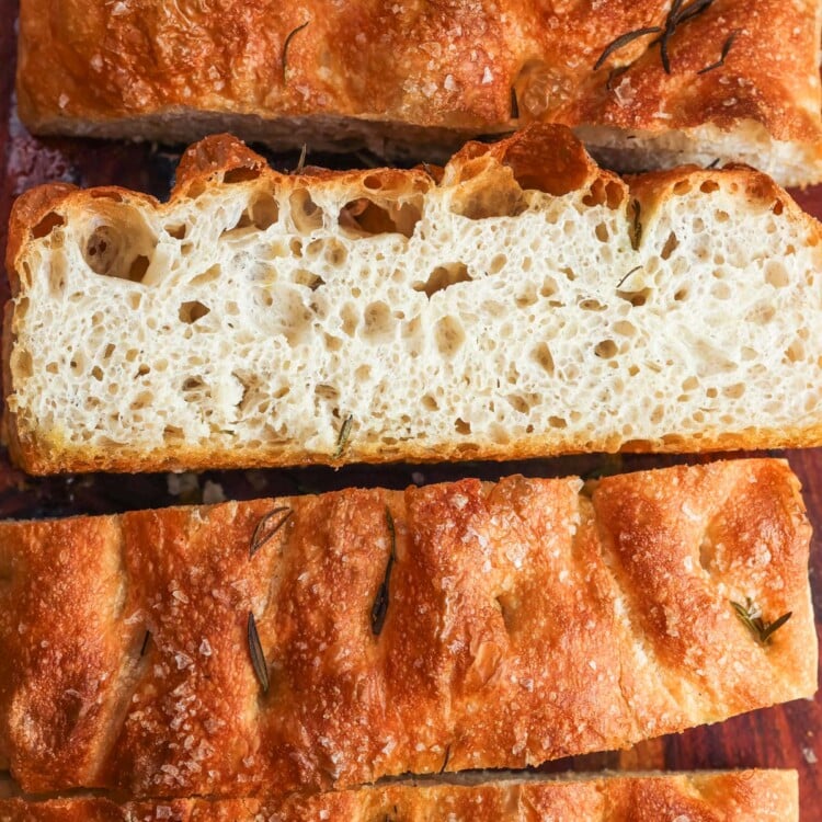 overnight focaccia cut into thick slices on a wooden board, showing an open airy crumb and dimpled crust