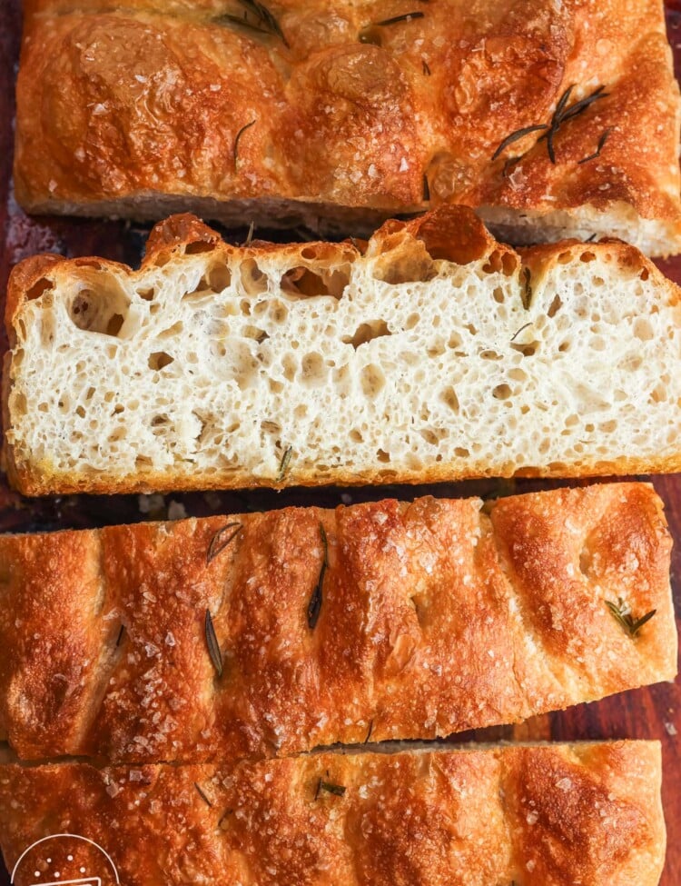 overnight focaccia cut into thick slices on a wooden board, showing an open airy crumb and dimpled crust