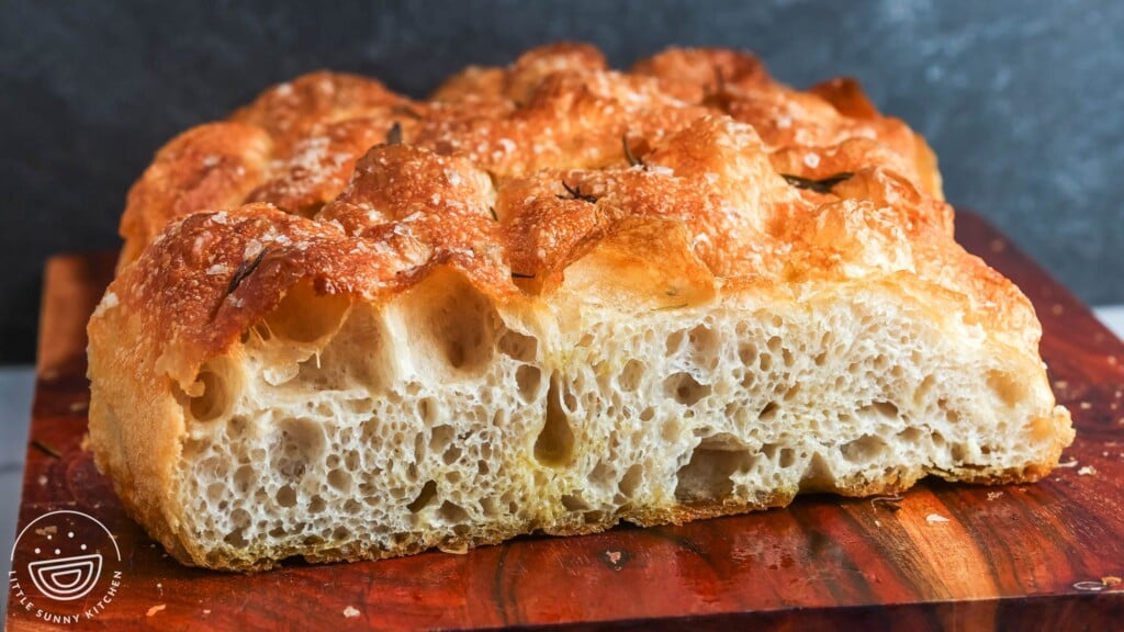 close up of a cut piece of focaccia with large air pockets and a crisp golden top with rosemary and salt.