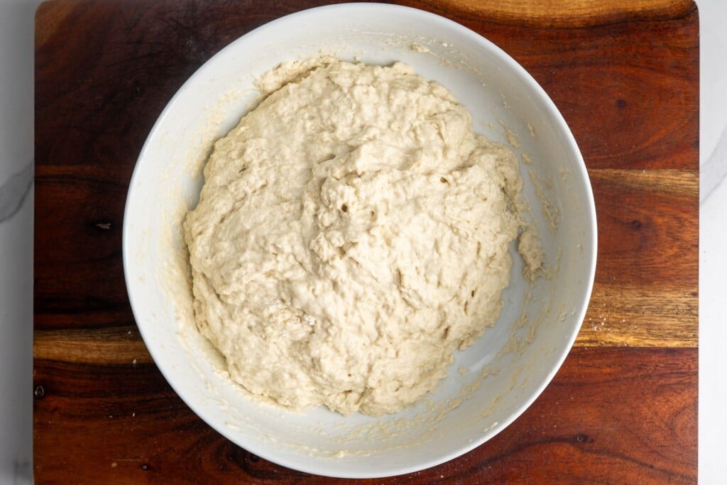shaggy, sticky focaccia dough in a white bowl, right after mixing. no dry flour is left in the bowl.