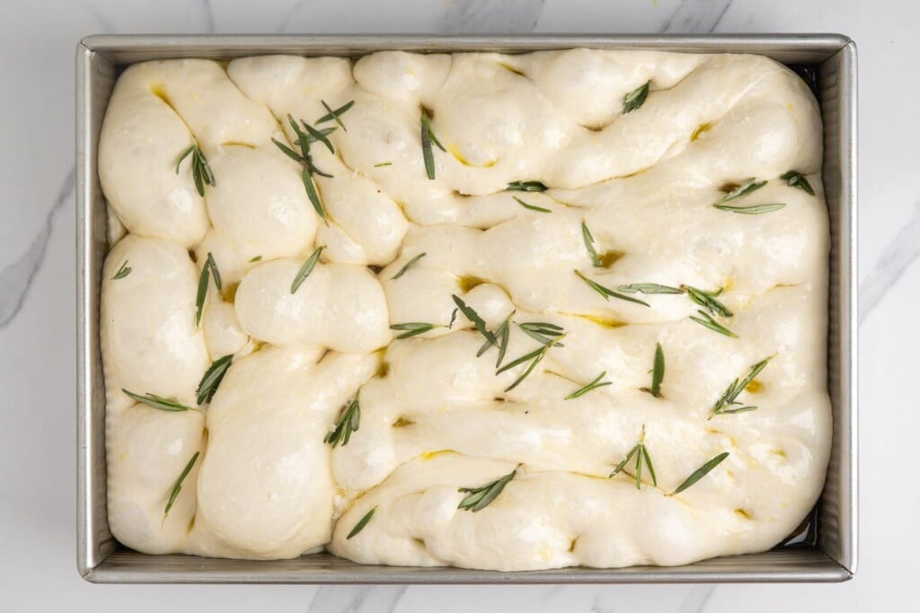 focaccia dough dimpled with fingertips and topped with olive oil, fresh rosemary, and flaky salt before baking.