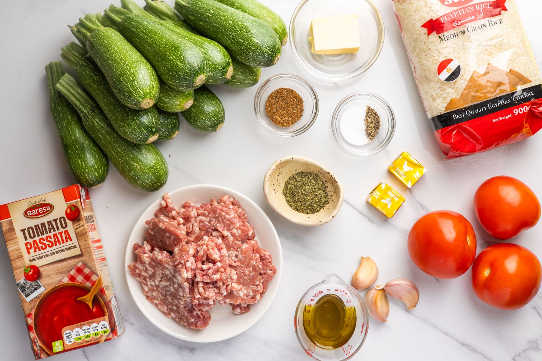 Ingredients for kousa mahshi, including small zucchini, rice, ground beef, tomatoes, tomato passata, stock cubes, garlic, spices and dried mint.