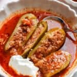 Kousa mahshi halved to show the rice and beef filling, served in tomato sauce with a dollop of yogurt.