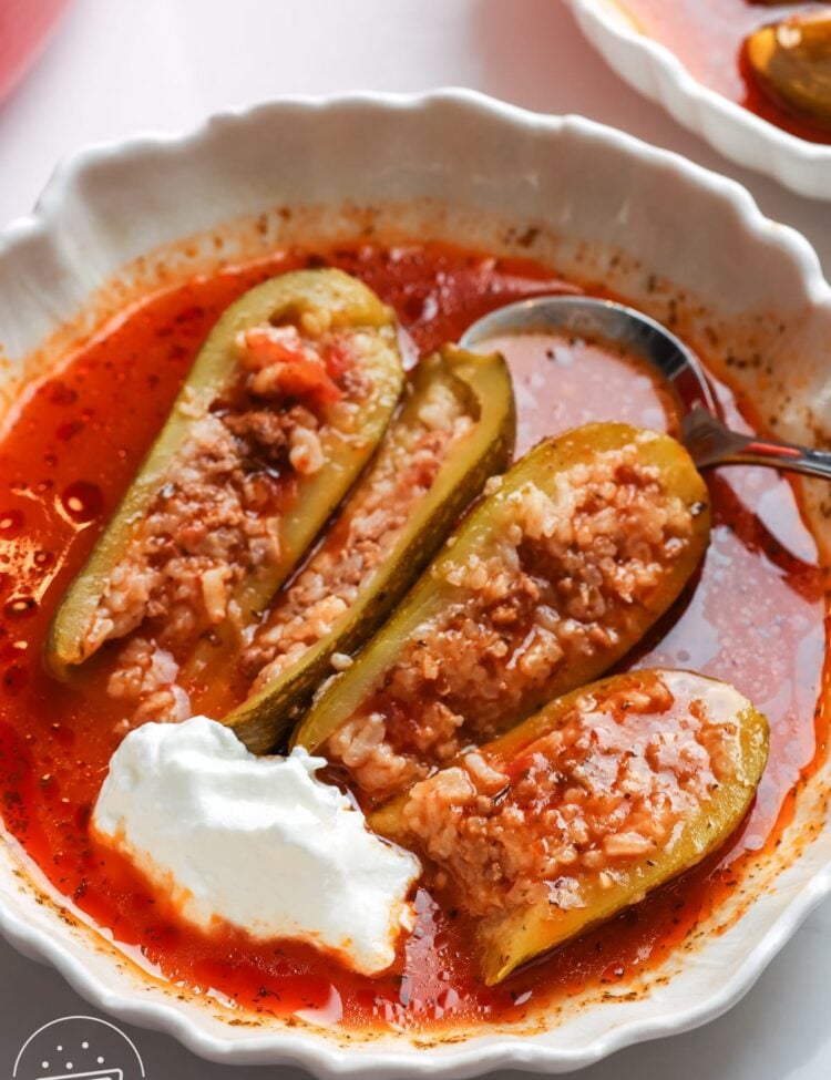 Kousa mahshi halved to show the rice and beef filling, served in tomato sauce with a dollop of yogurt.