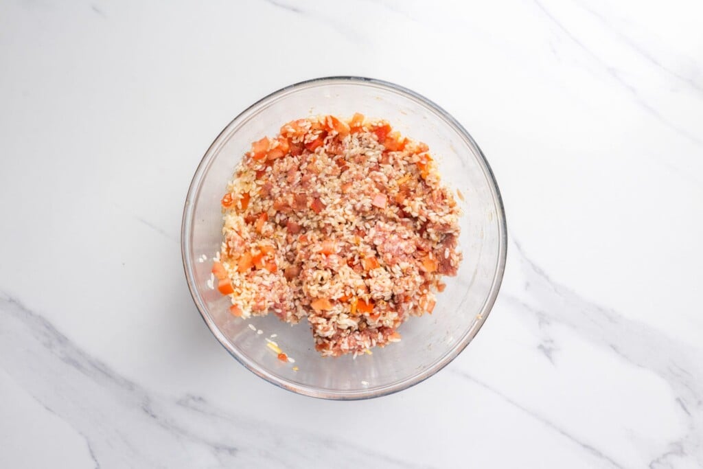 Rice, ground beef and diced tomato mixed together in a glass bowl for the filling.