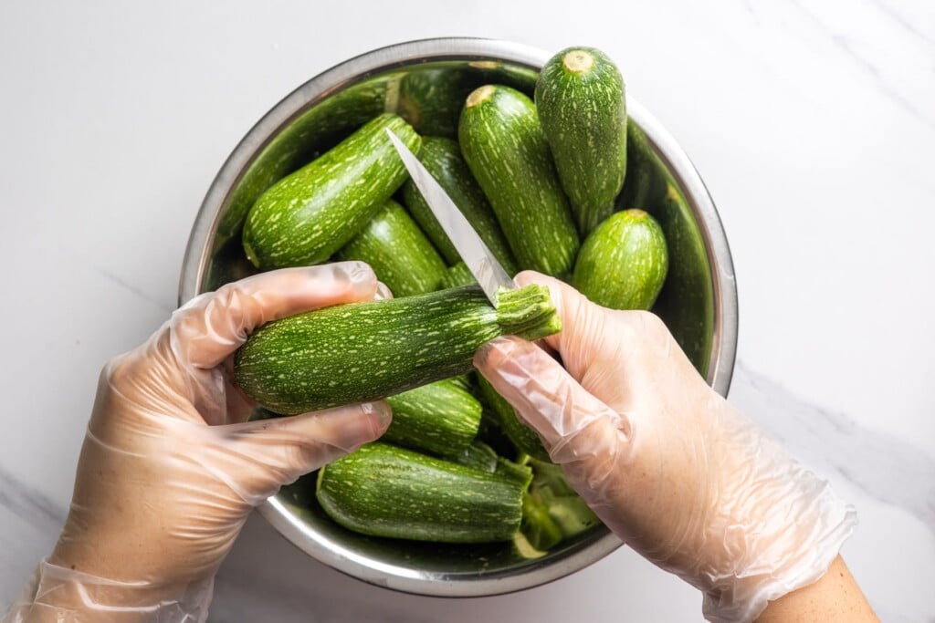Trimming the stem end off a zucchini with a small knife.