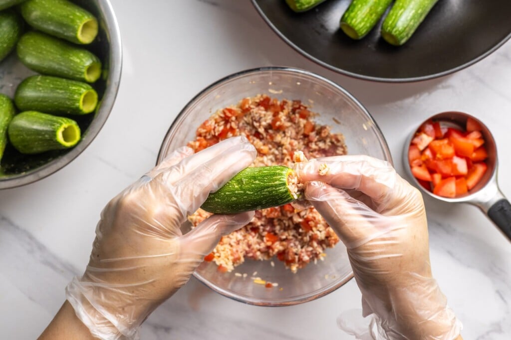 Stuffing a cored zucchini with the rice and meat filling.