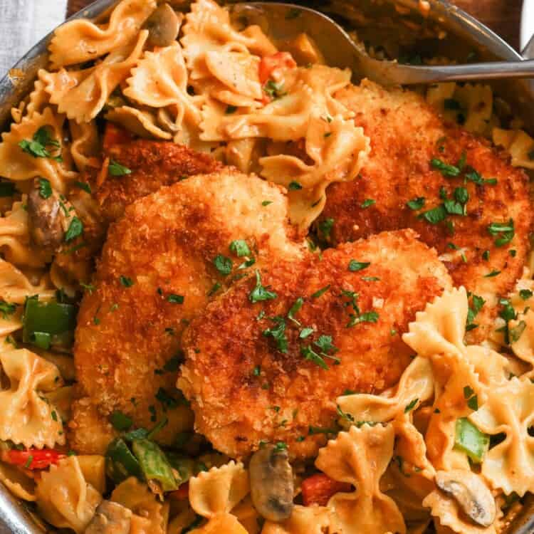 a skillet of louisiana chicken pasta with crispy cutlets, bowtie noodles, mushrooms and bell peppers.