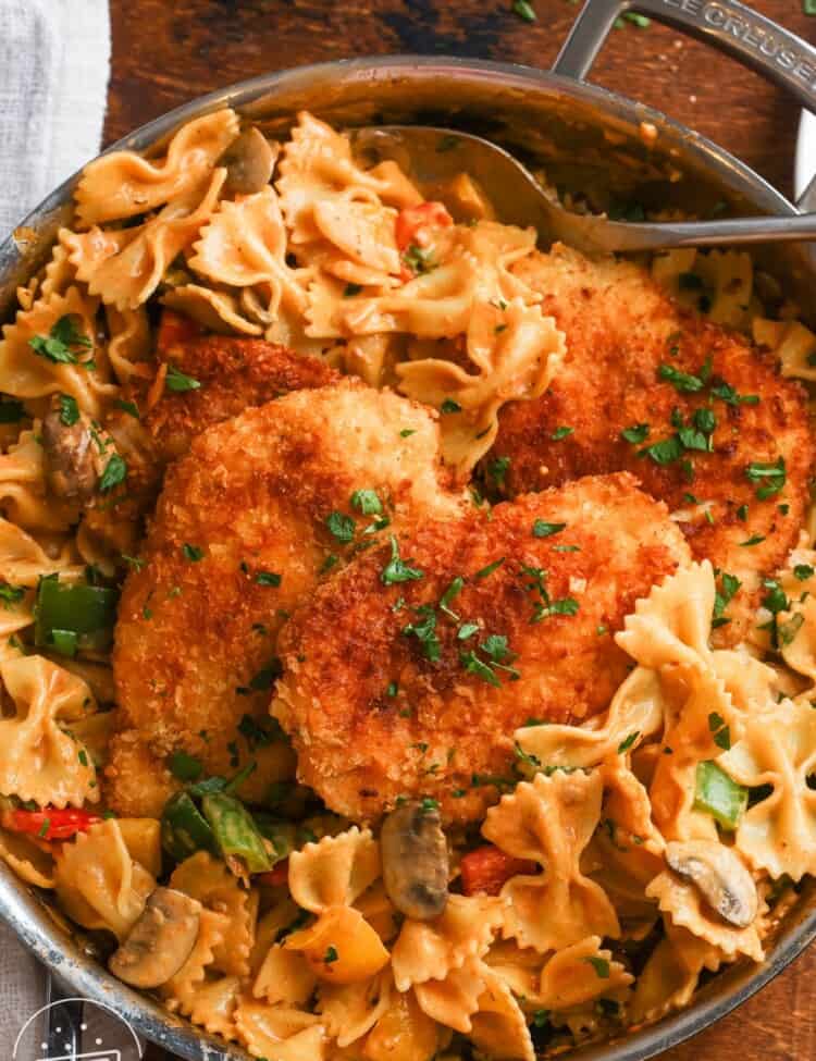 a skillet of louisiana chicken pasta with crispy cutlets, bowtie noodles, mushrooms and bell peppers.