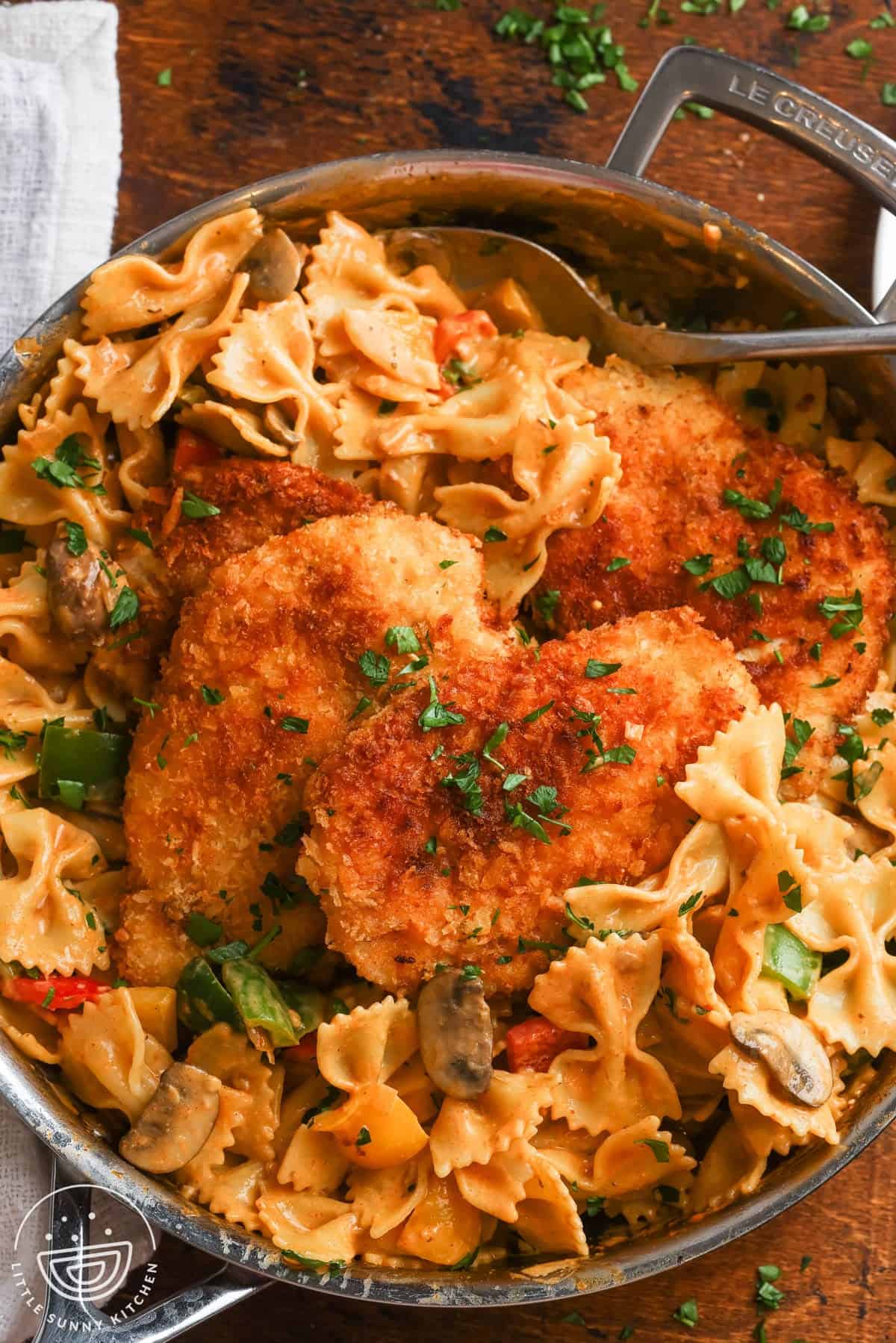 a skillet of louisiana chicken pasta with crispy cutlets, bowtie noodles, mushrooms and bell peppers.