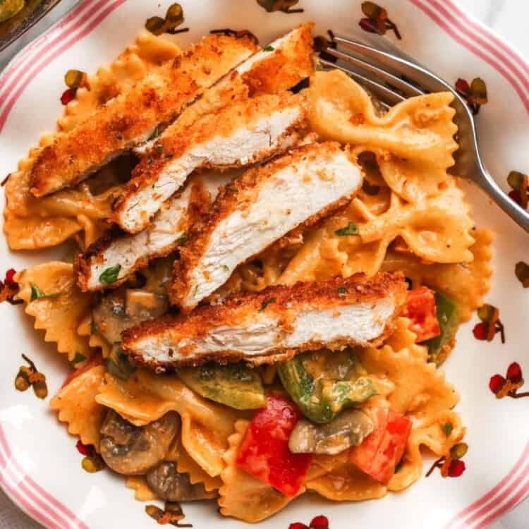 A plate of louisiana chicken pasta with sliced crispy chicken cutlet and pasta with peppers and mushrooms.