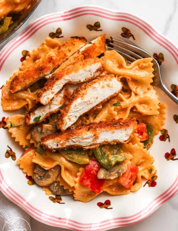 A plate of louisiana chicken pasta with sliced crispy chicken cutlet and pasta with peppers and mushrooms.