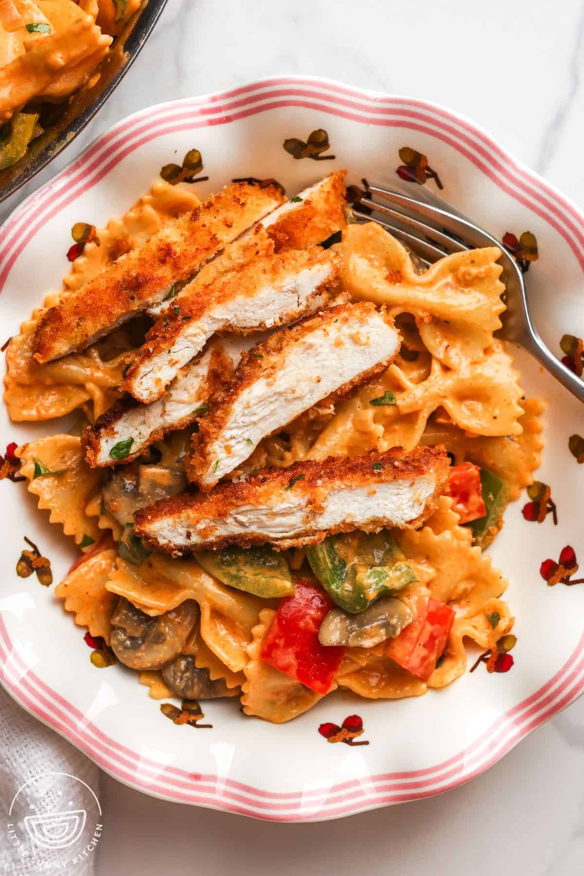 A plate of louisiana chicken pasta with sliced crispy chicken cutlet and pasta with peppers and mushrooms.