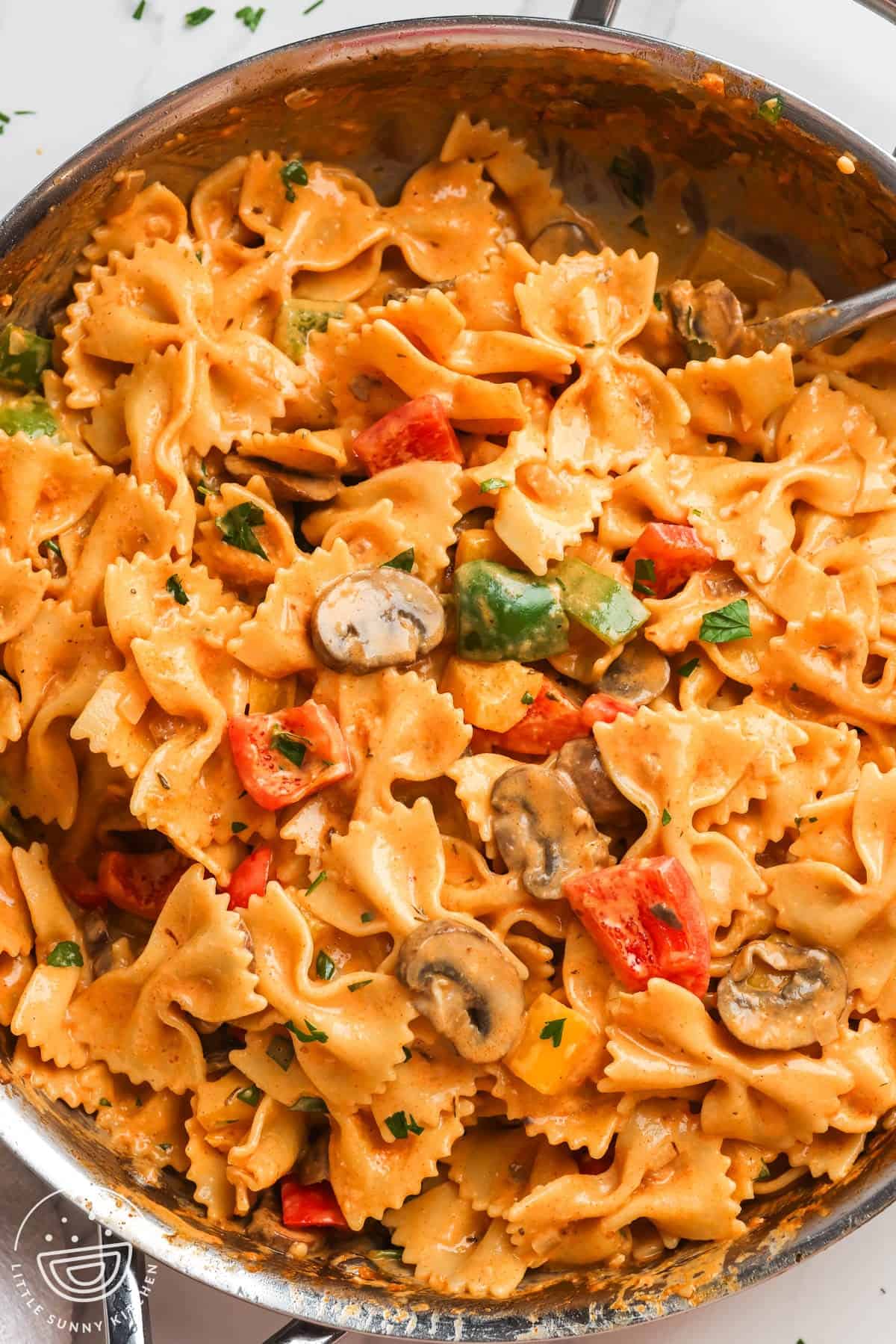 Bowtie pasta tossed with creamy sauce with mushrooms and peppers in a skillet for Louisiana chicken pasta