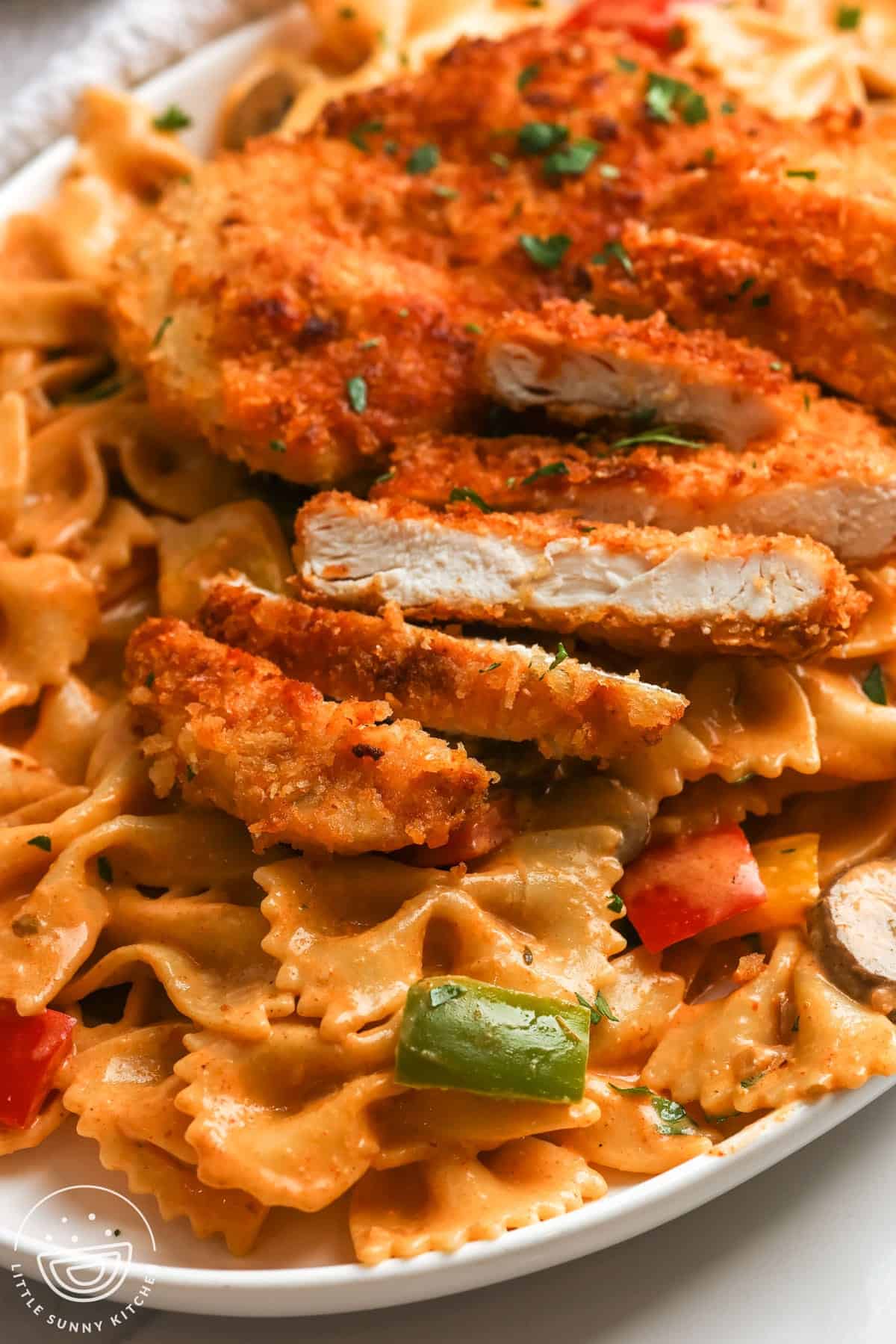 closeup of sliced crispy cajun chicken cutlet served over Louisiana pasta with veggies.