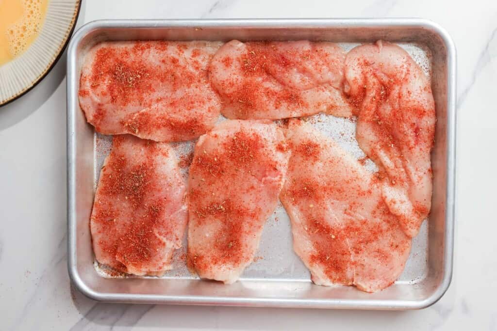 six chicken cutlets on a tray, seasoned with cajun seasoning.