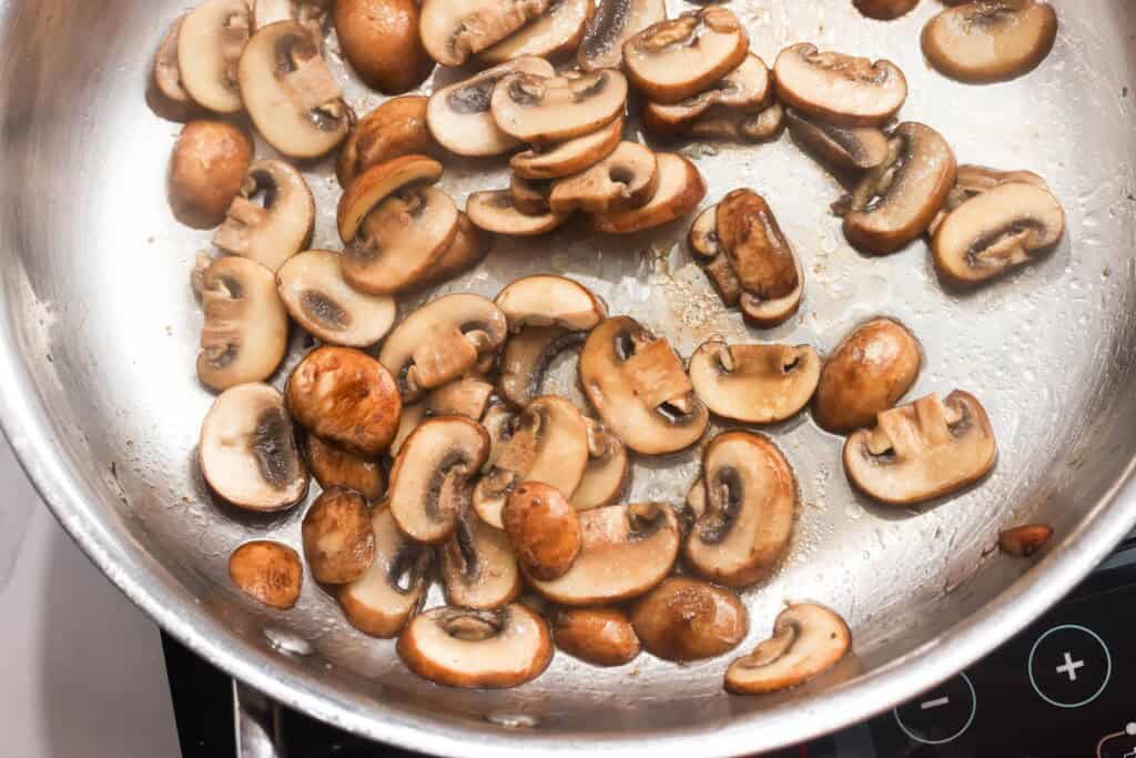 sliced cremini mushrooms cooking in a skillet.