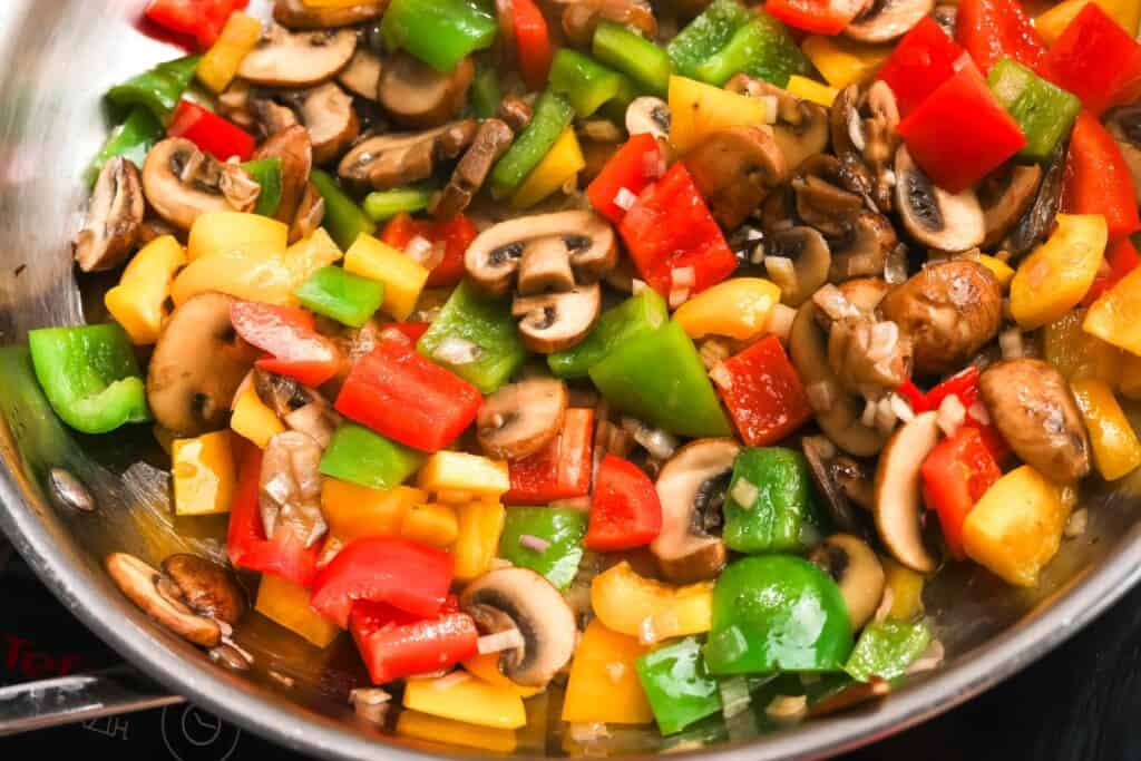 sliced mushrooms and colorful diced peppers cooking in a skillet.