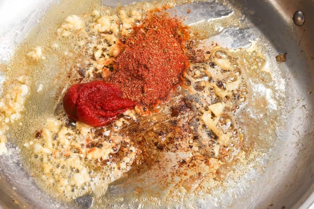 adding cajun seasoning and tomato paste to a skillet of sauteed garlic.