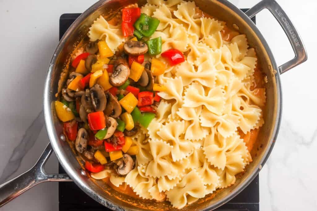 cooked bowtie pasta added to a skillet with cajun sauce and sauteed vegetables