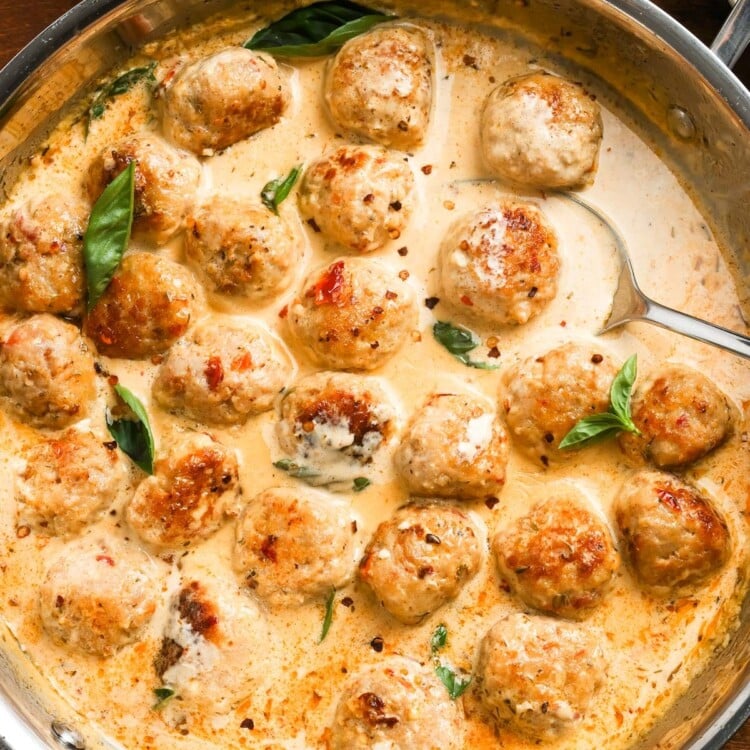 a skillet of saucy marry me chicken meatballs set on a wooden table.