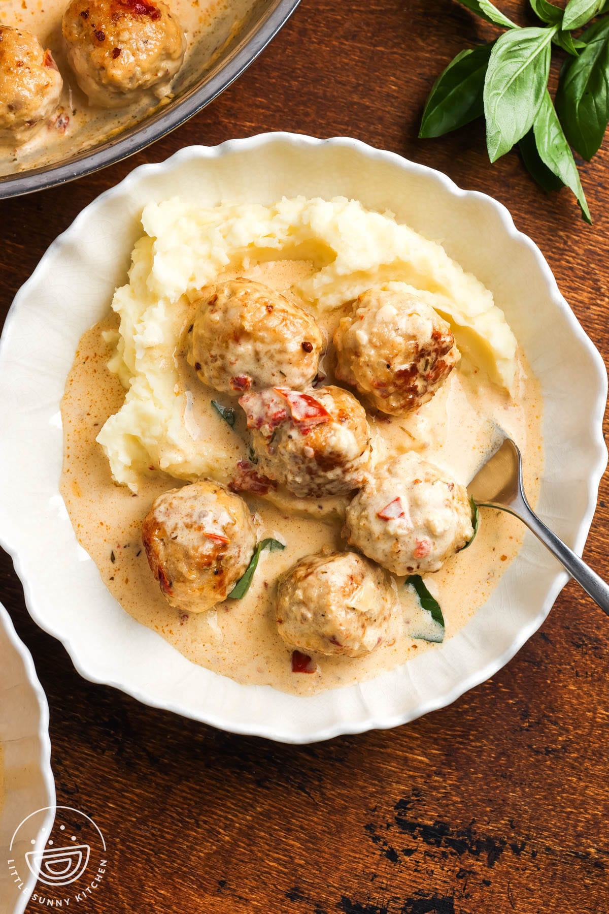 a white dinner plate of mashed potatoes topped with six marry me chicken meatballs and sauce.