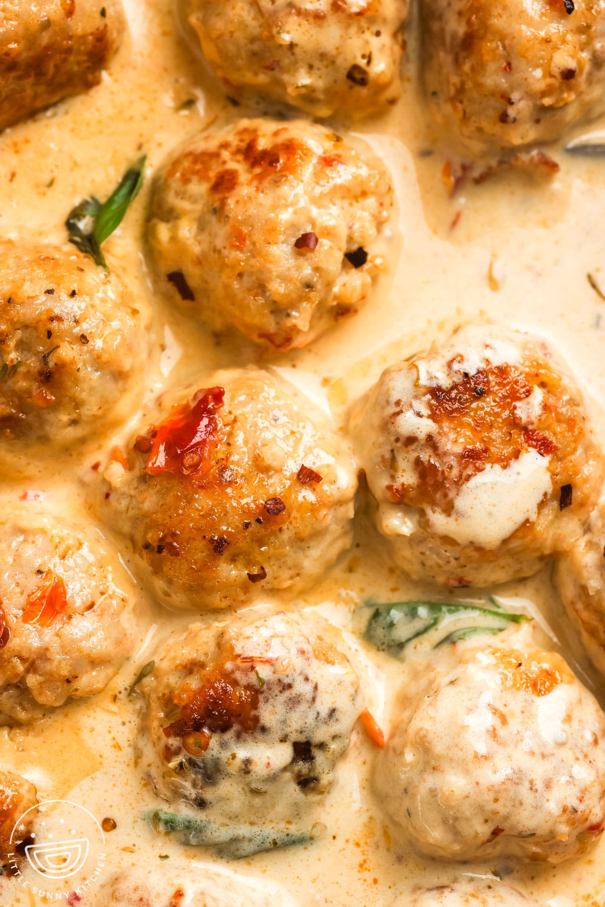 closeup of marry me chicken meatballs in a creamy sauce with basil and crushed red pepper flakes.