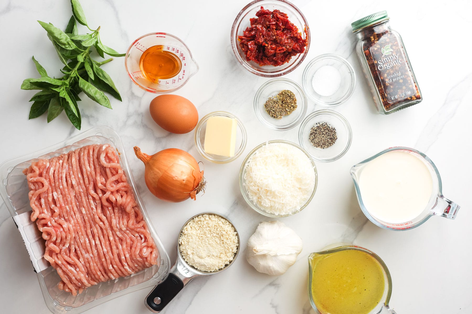 a pound of ground chicken with fresh basil, sun-dried tomatoes, and other ingredients for making marry me chicken meatballs. The ingredients are laid on a marble counter.