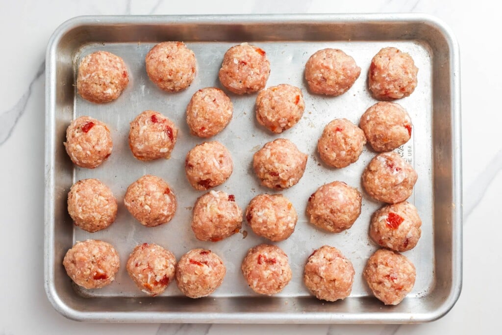 formed chicken meatballs on a metal baking pan.