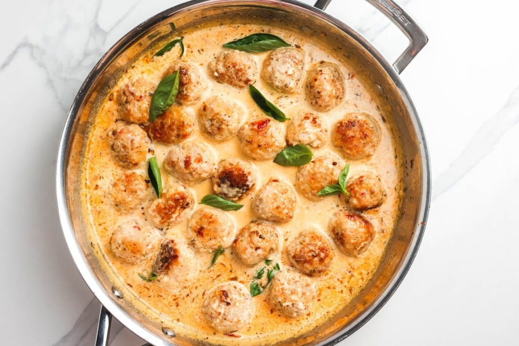 marry me chicken meatballs simmering in sauce, garnished with fresh basil leaves.