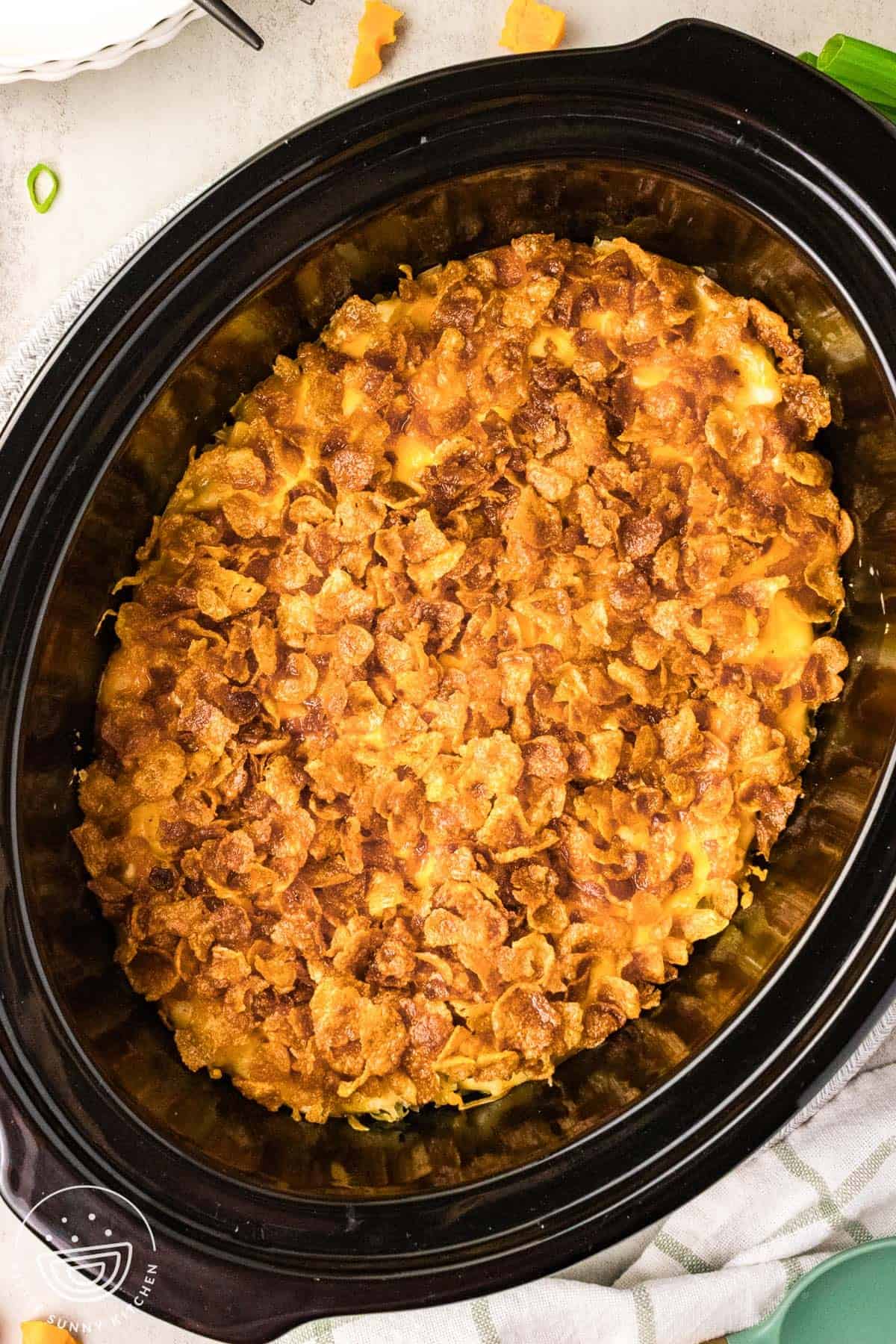 overhead view of cheesy potatoes with golden cornflake topping in an oval slow cooker.