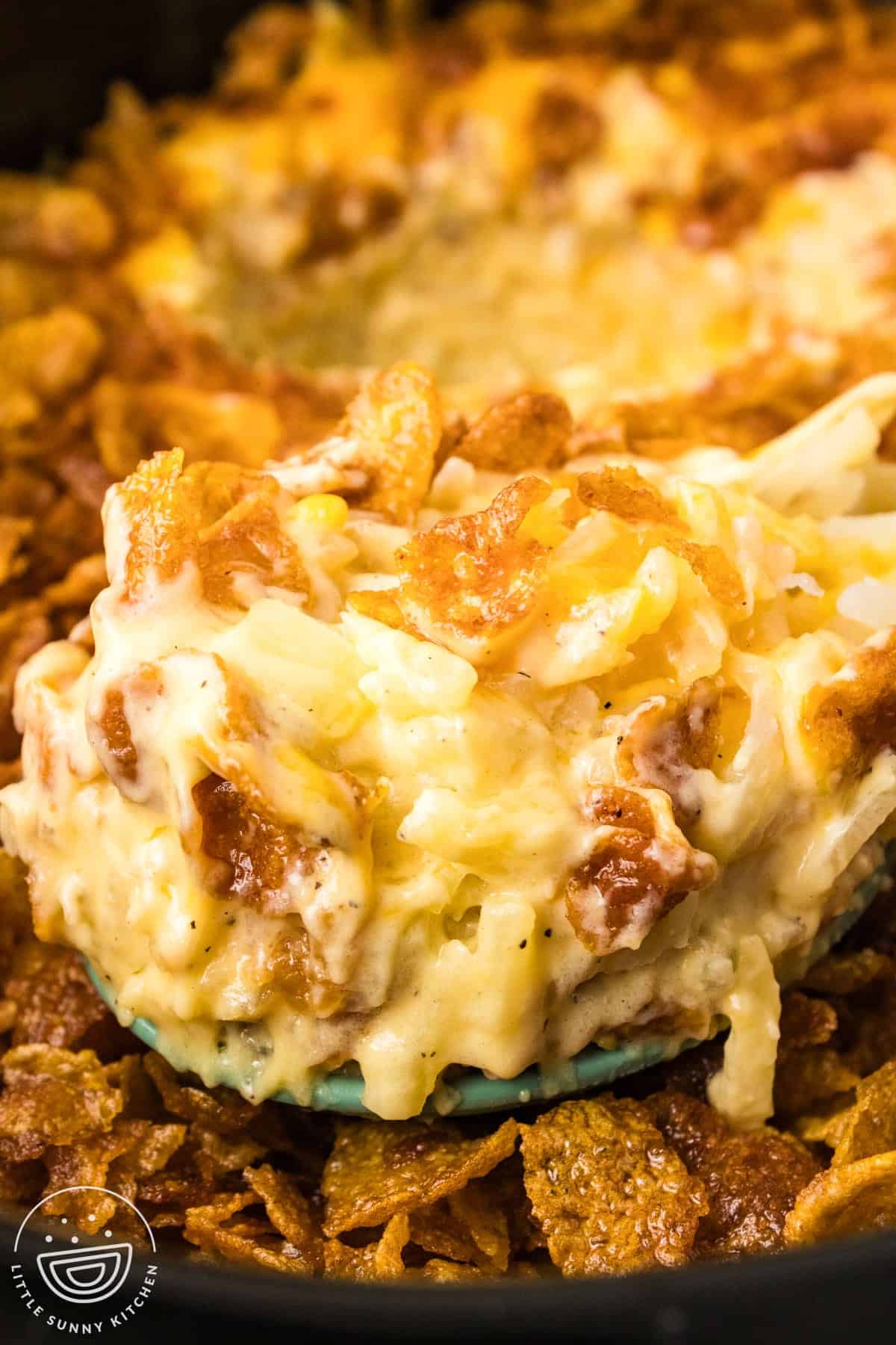 creamy cheesy hash brown potatoes with toasted cornflakes on a serving spoon.