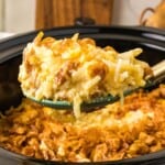 spoonful of crockpot cheesy potatoes lifted from a slow cooker, with crispy cornflake topping