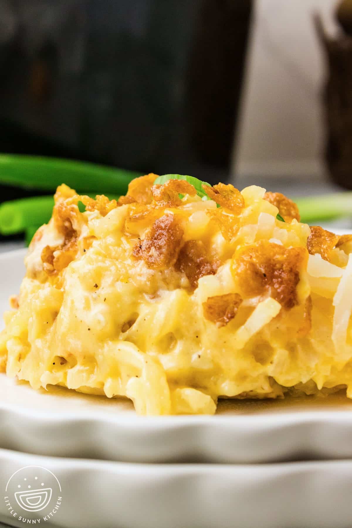 serving of cheesy hash brown potatoes on a white plate with green onions.