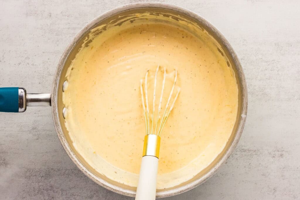 whisking cheese sauce for hash brown potatoes in a saucepan