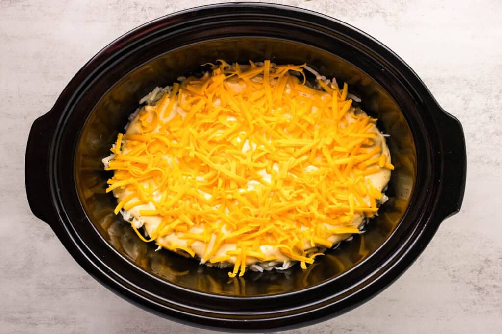 adding shredded cheese to hash browns in a slow cooker