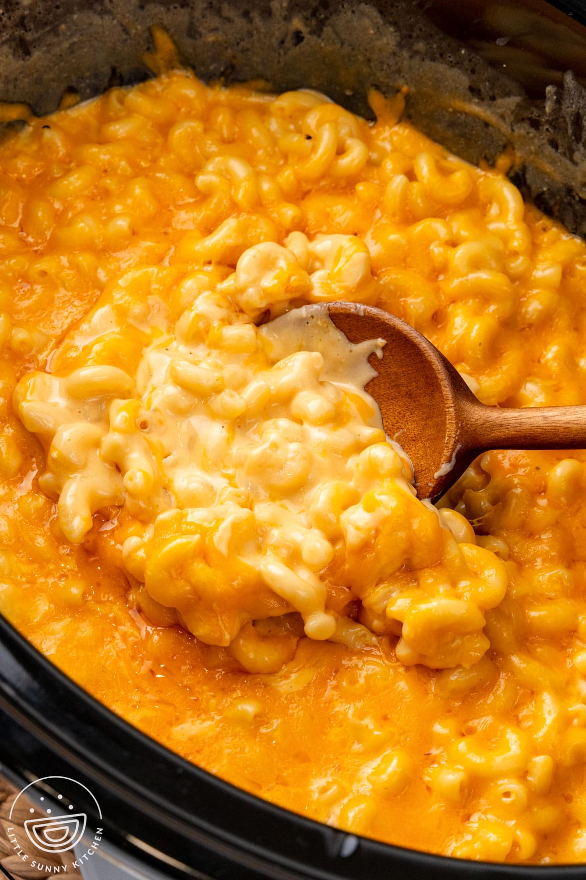 Mac and cheese cooked in a crockpot with a wooden spoon.