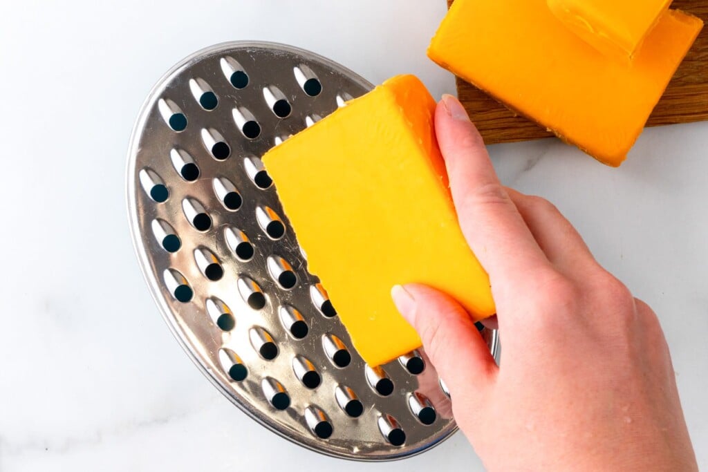 A block of cheddar cheese grated by hand on a metal grater.