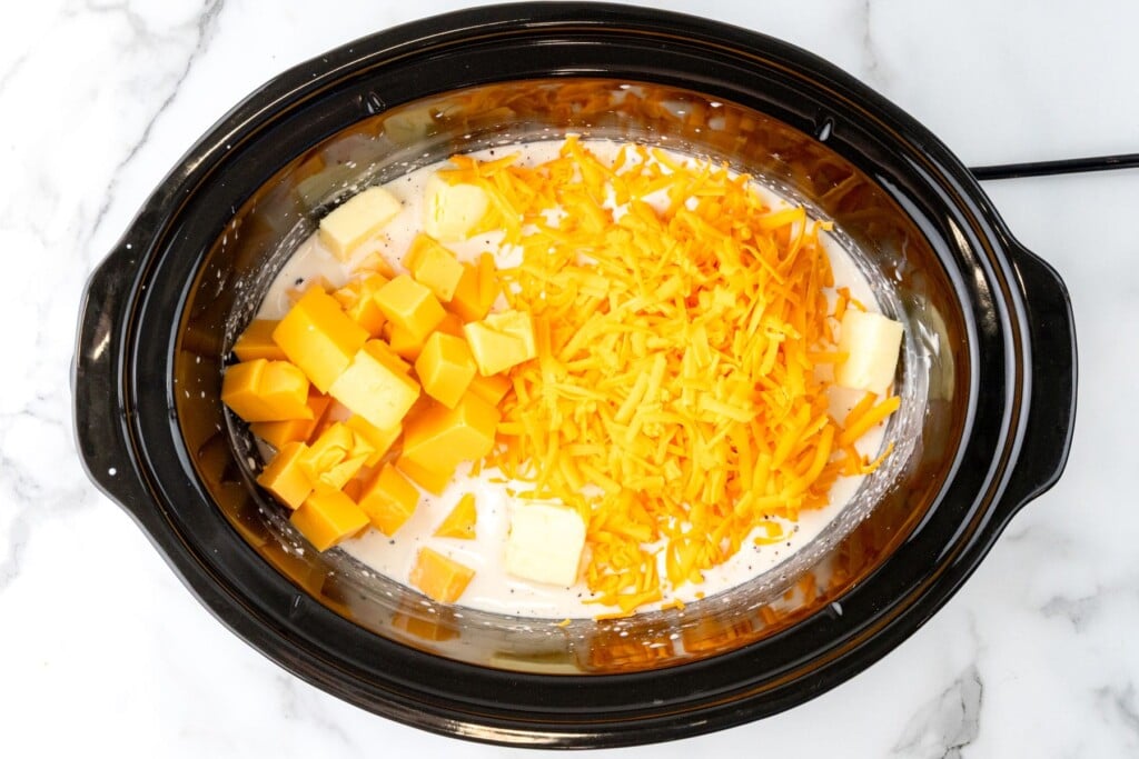 butter, cubes of velveeta and shredded cheddar added to a crockpot to make mac and cheese.