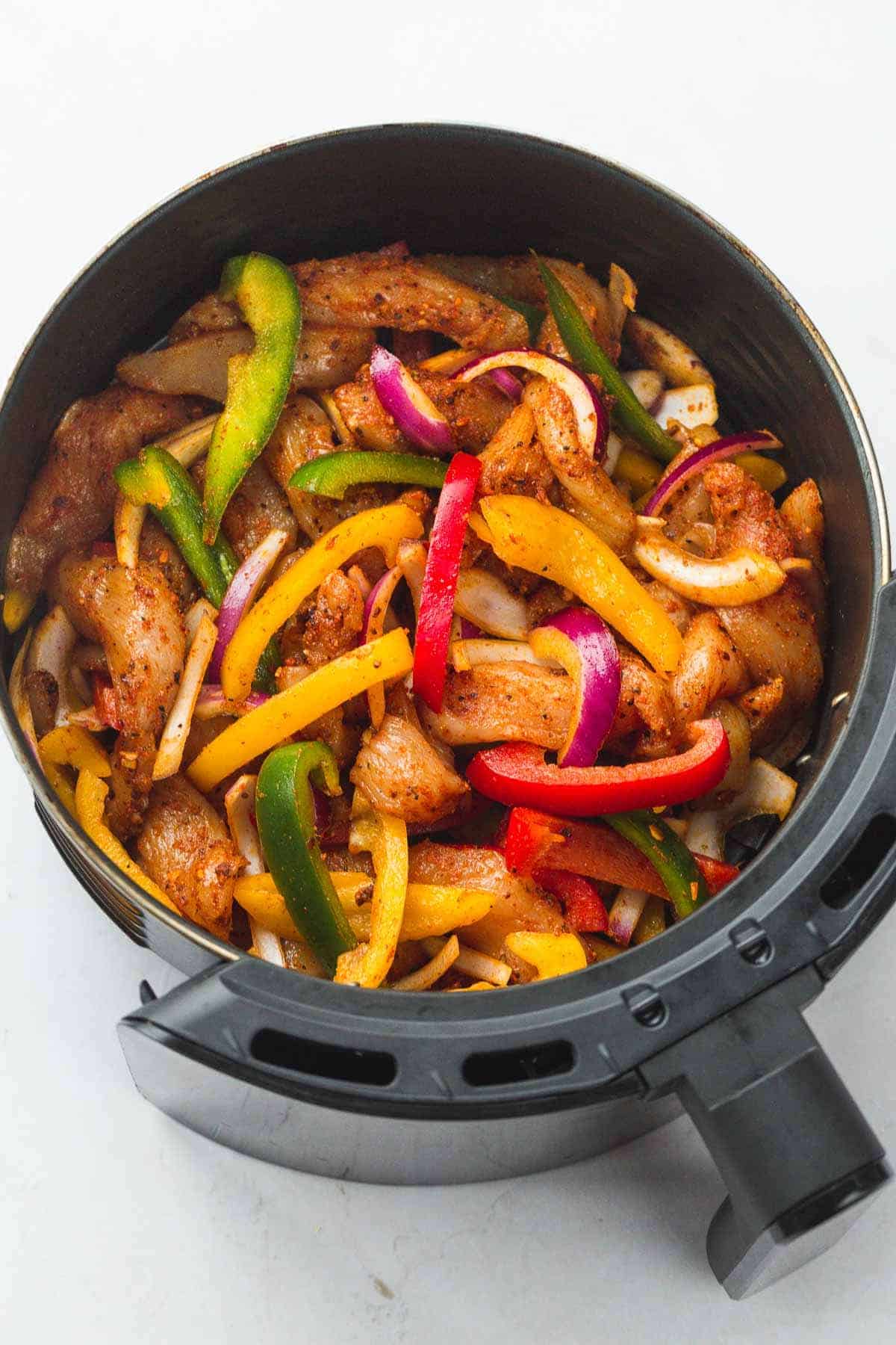 Raw chicken fajita strips and bell peppers in an air fryer basket.