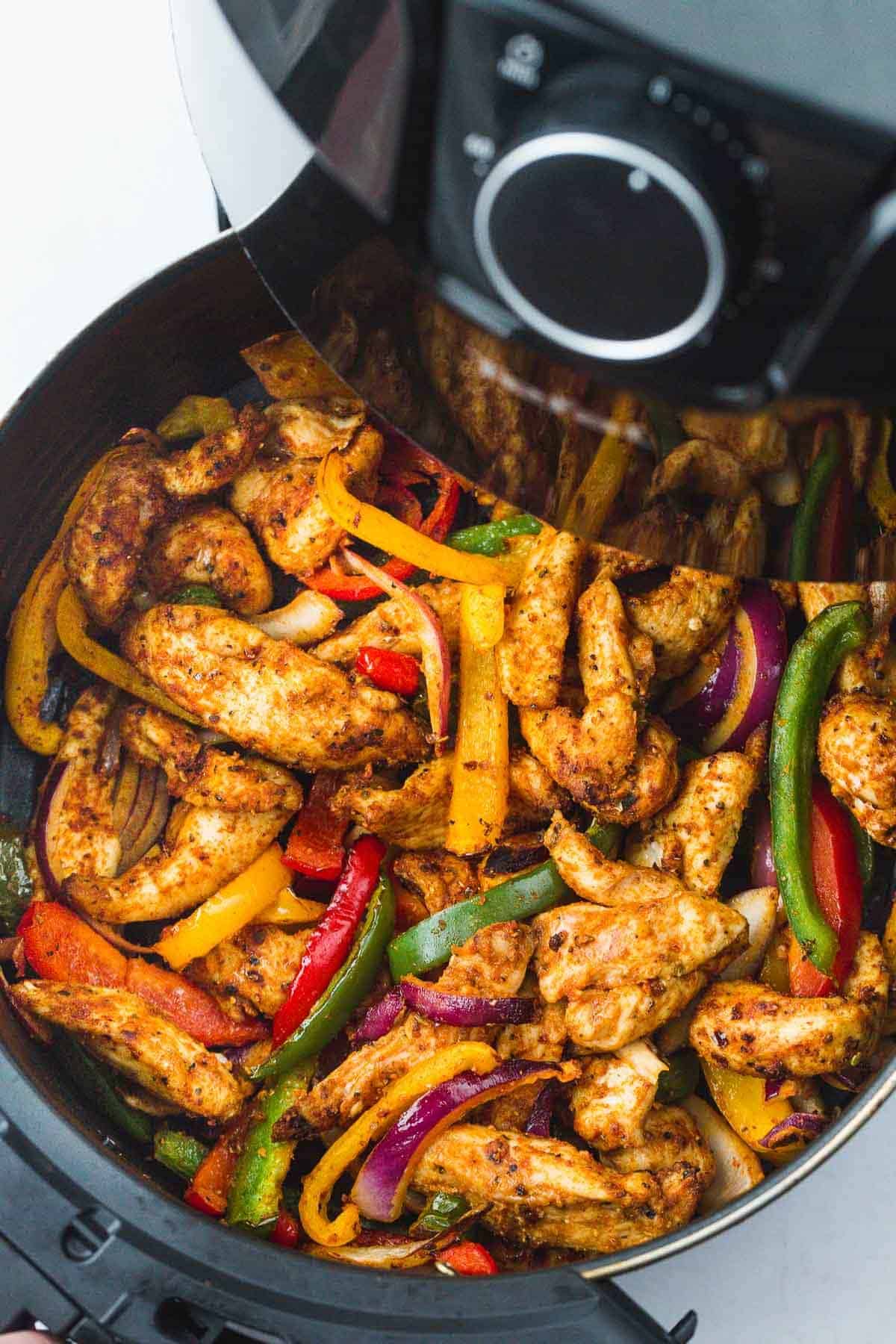 Chicken fajita strips and bell peppers in an air fryer basket.