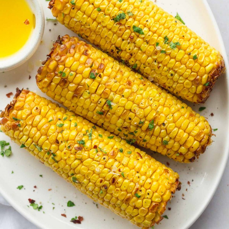 Air fryer corn on the cob with chopped parsley and seasoning on a plate