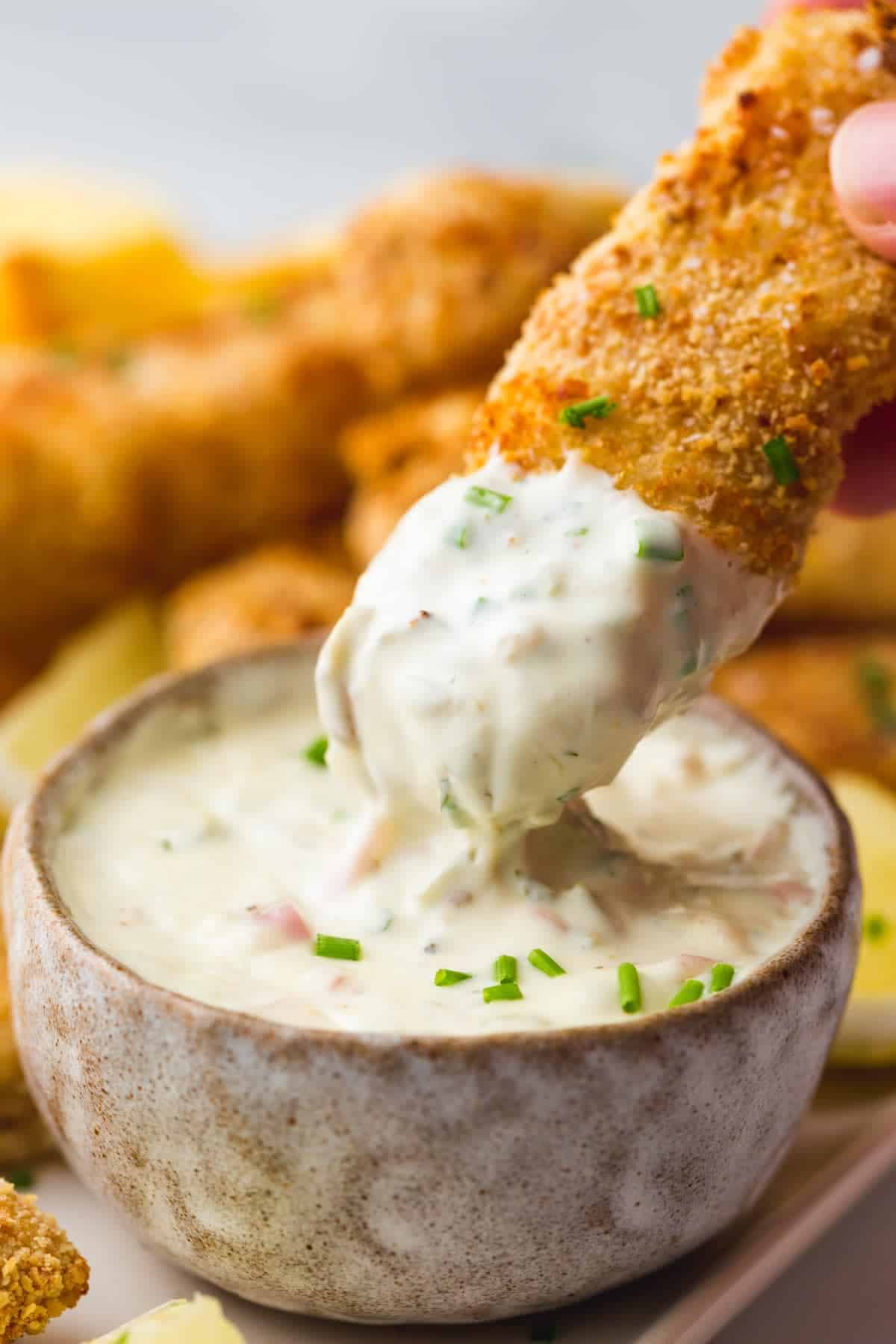 Dipping a fish stick in homemade tartar sauce, garnished with chives