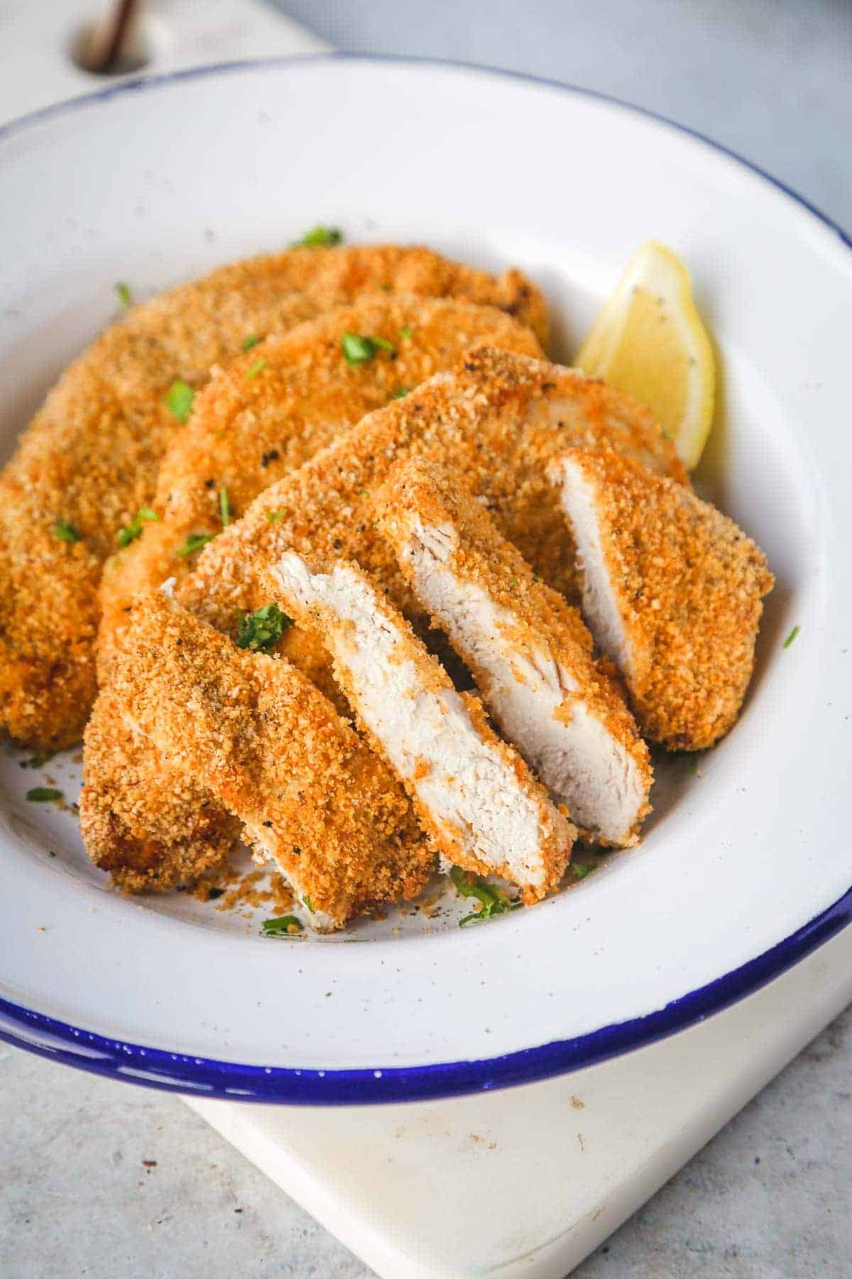 air fryer chicken breast, sliced and presented on a while plate with a lemon wedge