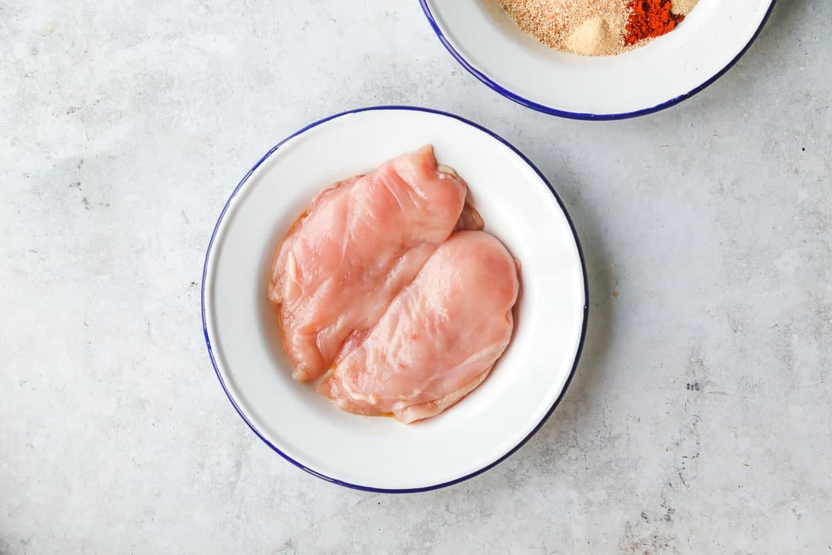 2 raw chicken breasts in a white plate